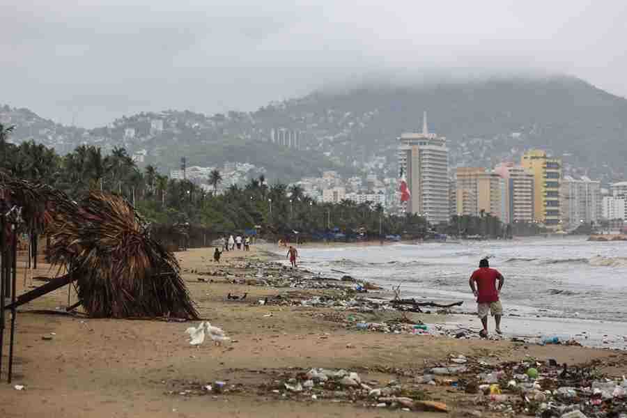 Personas caminan por una playa llena de basura debido a las fuertes lluvias hoy, en el balneario de Acapulco, estado de Guerrero (México). EFE/David Guzmán